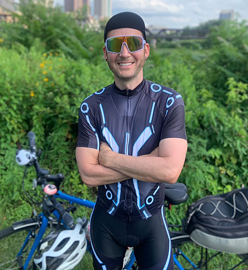 A male cyclist wearing a wulibike TRON short-sleeved kit crosses his arms over his chest and looks at the camera